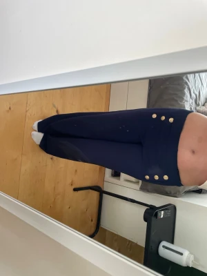 Mörkblå byxor med guldknappar - Snygga mörkblå byxor med hög midja och dekorativa guldknappar framtill i två rader. Byxorna har en rak och lite vidare passform som ger en trendig siluett. Perfekta för dig som vill sticka ut med detaljer och stilren look.