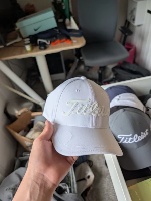 Vit keps från Titleist - Snygg vit keps från Titleist med broderad logga framtill. Klassisk böjd skärm och justerbar passform baktill. Tillverkad i ett lätt och ventilerande material som passar perfekt för golf eller andra utomhusaktiviteter.