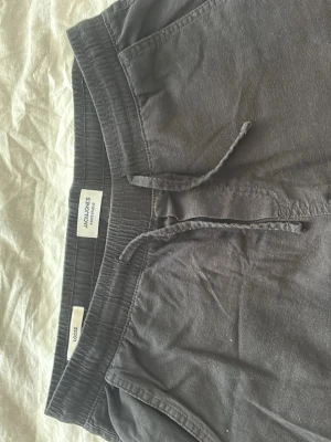 Mörkblå/svarta linnebyxor från Jack & Jones - Snygga svarta linnebyxor från Jack & Jones med dragsko i midjan och sidofickor. Perfekta för en avslappnad och stilren look. Byxorna har elastisk midja och är tillverkade i ett lätt och luftigt material. Pris kan diskuteras vid snabb affär. Skickar samma dag eller dagen efter.