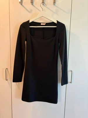Långärmad klänning, Nelly - Säljer en svart, kort klänning från Nelly med lång ärm och fyrkantig urringning, klänningen är i ett stretchigt material och är använd endast ett fåtal gånger. 