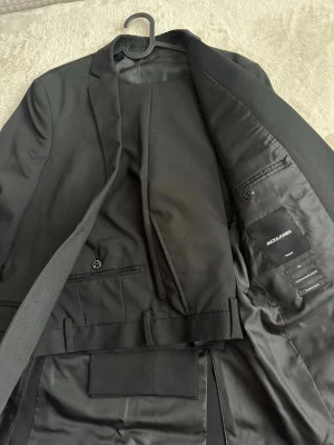 PREMIUM kostym från Jack & Jones, Super Slim  - PREMIUM Super Slim Jack & Jones kostym, dyrare än deras standard modell.                                                     Kavajen har två knappar, smala slag och innerfickor. Kostymen är i klassisk svart nyans och har använts vid 1 tillfälle i 3 h. Så gott som ny. 