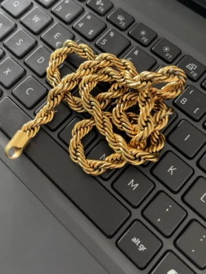 Guldfärgat tvinnat halsband - Säljer ett snyggt guldfärgat halsband med tvinnad kedja. Halsbandet har en robust och glansig finish som ger en lyxig känsla. Perfekt accessoar för att lyfta din outfit med en trendig touch. Rätt så tjock och är INTE äkta guld.