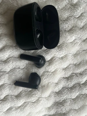 Svarta trådlösa in-ear hörlurar - Snygga svarta trådlösa in-ear hörlurar med laddningsetui. Hörlurarna har en stilren och kompakt design med rundade kanter och mattsvart finish. Perfekta för musik, poddar eller samtal på språng. Laddningsfodralet är smidigt att ta med i fickan eller väskan.