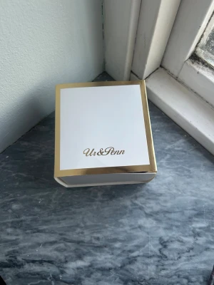 Guldfärgad klocka från Ur&Penn - Stilren guldfärgad klocka från Ur&Penn med rektangulär urtavla och klassiskt armband i metall. Urtavlan är vit med svarta romerska siffror och tunna visare. Perfekt accessoar för att lyfta din outfit.