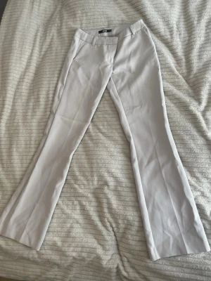 Vida ljusa kostymbyxor från Gina Tricot - Snygga kostymbyxor i ljusbeige från Bikbok med vida ben och pressveck. Byxorna har hällor för skärp, fejk fickor där bak och klassisk midja. Perfekta för en clean och stilren look.