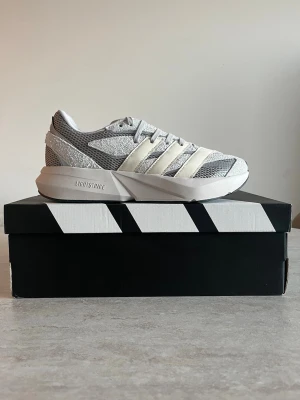Adidas grå sneakers med mesh och Lightstrike - Snygga sneakers från Adidas i grått och vitt med mesh-ovandel och klassiska tre ränder på sidan. Skorna har en chunky sula med Lightstrike-teknologi för extra komfort och sportig look. Perfekta för dig som gillar stilrena och moderna sneakers.