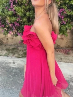  Ny trendig Axelbandslös rosa volangklänning - Superfin axelbandslös kort klänning i stark rosa färg med volangdetaljer upptill. Klänningen har ett plisserat tyg som ger ett luftigt och flowigt intryck. Perfekt för sommarens alla tillfällen!