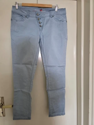 Ljusblå jeans med knappar - Snygga ljusblå jeans med fem knappar framtill och klassiska fickor både fram och bak. Jeansen har en smal passform och är tillverkade i ett mjukt denimtyg. Perfekta för dig som gillar en avslappnad men trendig stil.