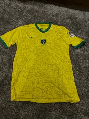 Brasilien matchtröja Rodrygo #10 - Gul Brasilien matchtröja från Nike med gröna detaljer och grafiskt mönster framtill. Landslagets emblem på bröstet, Rodrygo och nummer 10 på ryggen samt turneringsmärke på ärmen. Perfekt för fotbollsfans som vill sticka ut på planen.