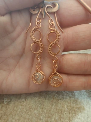 Handgjorda örhängen i ren koppar  - Unika örhängen i ren koppar, med spiralformade detaljer och hängande bergskristaller inneslutna i spiralen. Snyggt snirklig design som ger ett bohemiskt och kreativt intryck. Perfekta för dig som gillar handgjorda accessoarer med personlig touch och/eller vill ta del av kopparens spännande energi 🌀