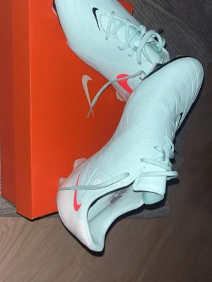 Nike Phantom GX mintgröna fotbollsskor - Snygga mintgröna Nike Phantom GX fotbollsskor med rosa och svarta detaljer. Skorna har en modern design med rundade linjer på ovandelen och klassisk snörning. Tillverkade i syntetmaterial för bra grepp och känsla på planen. Perfekta för dig som vill sticka ut på matchen. Inte använd en enda gång säljs på grund av för stor storlek butik pris är 1500 kr 