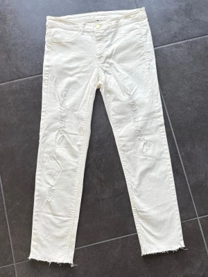 Offwhite slim jeans med slitningar - Offwhite vita jeans med slitna detaljer framtill och råa kanter vid bensluten. Modellen är slim fit med normalhög midja och femficksdesign. Längd ca 84 cm, innerbenslängd ca 60 cm.