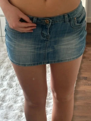 Lågmidjad minikjol - Säljer en blå jeansminikjol från Monday denim med klassisk femficksdesign och knappstängning framtill. Kjolen har en kort passform och är tillverkad i denim med snygga slitningar och ljusa partier. Perfekt för dig som gillar en trendig och avslappnad look. Jättebra skick. Storlek 38 men liten i storlek 