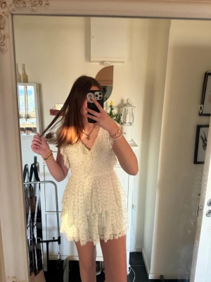 Vit spetsklänning med volang - Söt vit kortklänning med spets och volangdetaljer. Klänningen har v-ringning, korta ärmar och knyt i ryggen. Perfekt för sommarens alla tillfällen och ger en romantisk vibe. Materialet är lätt och luftigt, vilket gör den bekväm att bära. Köpt för 609kr