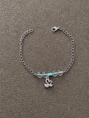 Silverfärgat armband med blå pärlor -  armband med silverfärgad kedja, med ljusblå genomskinliga pärlor och små turkosa. Armbandet har ett hängsmycke i form av en svan 