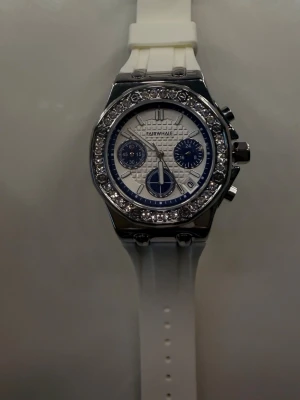 Vit klocka med kristaller Mark Fairwhale - Snygg vit klocka från Mark Fairwhale med silvrigt boett och gnistrande kristaller runt urtavlan. Klockan har flera knappar på sidan och ett sportigt, modernt utseende. Levereras i original blå box.  ALDRIG ANVÄND. Nypris 1000 kr