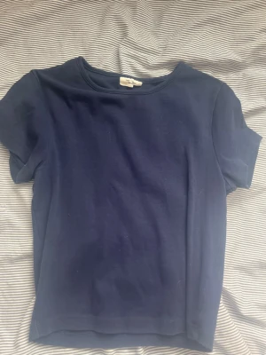 Mörkblå basic t-shirt från Banana Republic - En enkel och stilren mörkblå t-shirt från Banana Republic. T-shirten har rund halsringning och korta ärmar. Tillverkad i mjuk bomull som känns skön mot huden. Perfekt till jeans eller shorts för en clean look.