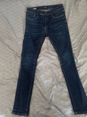 Mörkblå skinny jeans från Cheap Monday - Säljer ett par mörkblå skinny jeans från Jack And Jones med klassisk femficksdesign och snygga slitningar vid knäna. Jeansen har en smal passform och är tillverkade i stretchigt denim som sitter bekvämt. Perfekta för dig som gillar en modern och tight look. Storlek w30, L-31