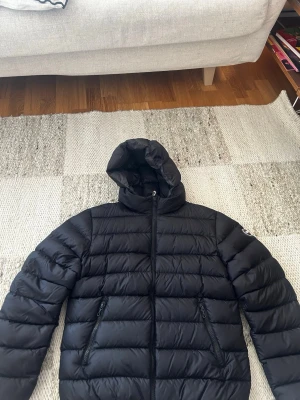 Svart dunjacka med huva Colmar - Säljer en svart dunjacka från Colmar med huva och två dragkedjeförsedda fickor. Jackan är i bra skick, endast en liten del av märket i bak som fallit bort annars är den så gott som ny. Jackan passar dig som är mellan 165-170. Skriv gärna vid fler funderingar.
