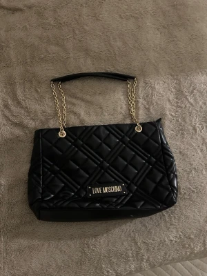 Love moschino väska - Love moschino väska Säljer en Moschino väska, den kommer även med skyddspåsen, påsen har någon fläck och i väskan finns även lite fläckar som går att tvättas ur. Väldigt fint och passande för dig med stockholm stil eller allmänt baddie.