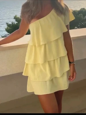  Ny  slutsåld Gul offshoulder volangklänning - Söt gul kortklänning med offshoulder och flera lager volanger. Klänningen har en luftig passform och är perfekt för varma dagar. Tillverkad i ett lätt tyg som ger en somrig känsla.