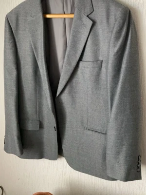 Klassisk grå kavaj med notch-lapel - Säljer en stilren grå kavaj med notch-lapel och två framfickor. Kavajen har slät finish och är helfodrad med grått innerfoder. Perfekt för dig som vill ha en enkel och tidlös look. Passar till skjorta eller t-shirt.