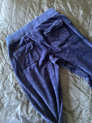 Blå velourmjukisbyxor med fickor - Mysiga blå mjukisbyxor i velour med bred resår i midjan och snörning. Byxorna har två bakfickor med lock och raka ben. Perfekta för chill eller häng med kompisar.