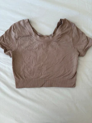 Beige ribbad croppad topp H&M Sport - Säljer en beige ribbad croppad topp från H&M Sport. Toppen har korta ärmar, rund halsringning och är tillverkad i ett mjukt stretchigt material som passar perfekt till träning eller chill. Enkel och stilren design som är lätt att matcha.