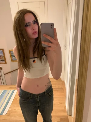 Vit croppad tubtopp med yin yang - Säljer en vit croppad tubtopp med svarta band och en liten yin yang-symbol framtill. Toppen är ärmlös och har en enkel, stilren design som passar perfekt till jeans eller kjol. Materialet känns mjukt och stretchigt, troligen bomull eller syntet.