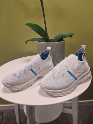 Vita somriga slip-on sneakers med Gant innesula, storlek 36 - Snygga vita slip-on sneakers med stickad ovandel och blå samt rosa detaljer på sidan. Skorna har en tjock vit sula och elastisk öppning som gör dem enkla att ta på. Perfekta för dig som gillar en sportig och modern look.