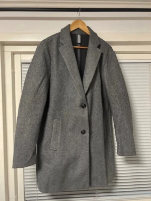 Grå ullrock från LCW Vision - Snygg grå rock från LCW Vision i storlek L. Rocken har klassisk rak passform, två knappar framtill och diskreta sidofickor. Materialet är ullblandning som ger en stilren look och håller dig varm. Perfekt för dig som gillar minimalistisk och tidlös stil.