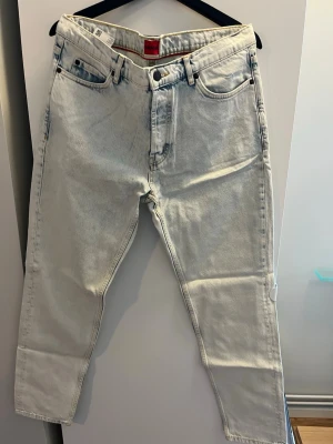 Ljusa jeans från Hugo Boss - Snygga ljusa jeans från Hugo Boss med klassisk femficksdesign och raka ben. Jeansen har en cool tvättad look och röda detaljer på insidan av linningen. Materialet är bomull och de har en modern passform. 33/34