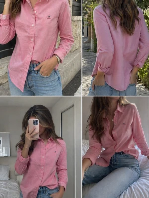 Rosa skjorta från Gant - Klassisk rosa skjorta från Gant i bomull med knappar framtill och liten broderad logga på bröstet. Skjortan har lång ärm, normal passform och en mjuk, bekväm känsla. Perfekt att styla med jeans för en avslappnad look. På femte bilden ser man att ena knappen vid handleden är halv, men det medföljer två knappar från Gant som enkelt kan bytas ut om man vill. 