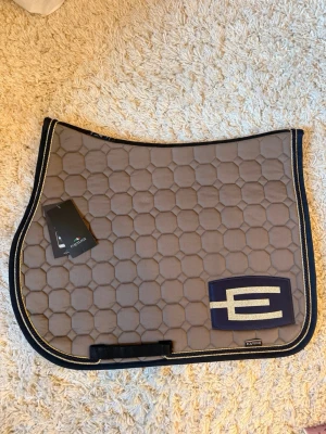 Unikt helt nytt Equiline schabrak😍  - Jättefint och helt oanvänt unikt Equiline schabrak med E-logga😍  Nypris: 2049kr, lappen sitter kvar❤️ Kostar 2444kr att designa själv på VB ridsport❤️  Storlek: Full Modell: Hopp/allround  Design⚜️: - cappuccino färg  - blå med guldglittrig E-logga  - 3 passpoaler (guld, blå, guld)   Air control systen och shock absorbtion.  Köpt på SIHS och är av begränsad upplaga (finns ej att köpa i butik)   Jättesnygg och perfekt alla årstider både på träning och tävling❤️  Skickas i säker förpackning eller häm