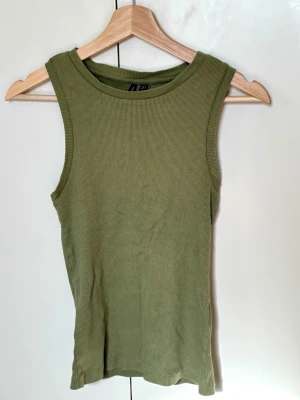 Olivgrön ribbad linnetopp från Vero Moda - Säljer en olivgrön ribbad linnetopp från Vero Moda. Toppen är ärmlös med rund halsringning och har en slim passform. Perfekt att matcha med jeans eller shorts för en avslappnad look.