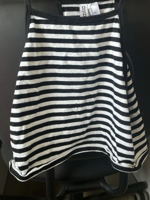 Randig linnetopp från Divided - Säljer en svartvit randig linnetopp från Divided. Toppen har smala axelband och är ärmlös med en enkel, rak passform. Perfekt för dig som gillar en clean och stilren look. Materialet är mjukt och känns bekvämt mot huden.