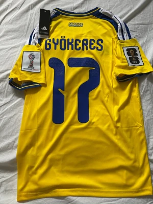 Sverige VM-hemmatröja, Gyökeres nr 17 - Sveriges VM-hemmatröja med gyökeres nummer 17 på ryggen. Tröjan är helt ny med VM loggorna på axlarna. Tröjan är från adidas i storlek S.