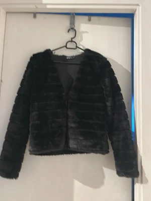 Svart pälsjacka från Gina Tricot - Säljer en svart, kort pälsjacka från Gina Tricot. Jackan har en rak passform, långärmad design och är gjord i mjukt fuskpälsmaterial med horisontella paneler. Perfekt för att ge din outfit en lyxig touch.