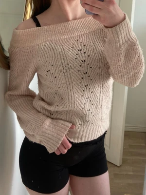 Beige off shoulder stickad tröja - Säljer en beige stickad tröja med off shoulder-design och snyggt hålmönster. Tröjan har bred ribbad kant vid halsen och långa ärmar. Perfekt för dig som gillar en avslappnad och trendig look.