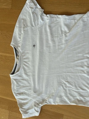 Vit t-shirt från GANT i bomull - Klassisk vit t-shirt från GANT med rund hals och diskret logga på bröstet. Tillverkad i mjuk bomull och har korta ärmar. Perfekt basplagg för en clean och enkel stil.