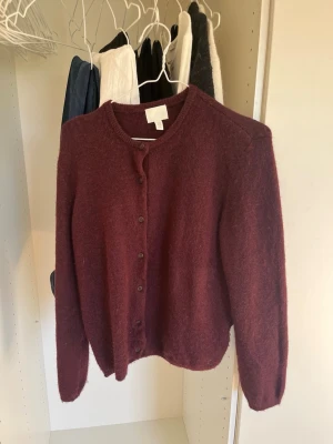 Vinröd kofta från H&M, XS - Mysig vinröd kofta från H&M i storlek XS. Koftan har rund halsringning, knappar framtill och är tillverkad i ett mjukt, luddigt material. Aldrig använd