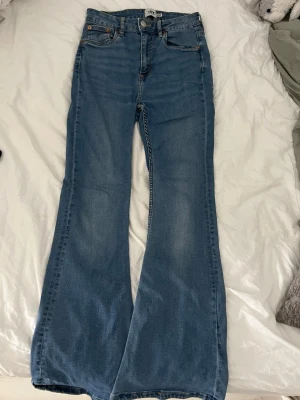 Blå utsvängda jeans från Lager 157 - Säljer ett par blå utsvängda jeans från Gina Tricot med klassisk femficksmodell och hög midja. Jeansen har en snygg tvätt och är tillverkade i denim med lätt stretch. Perfekta för dig som gillar retrostil och vill ha ett par bekväma och trendiga jeans.