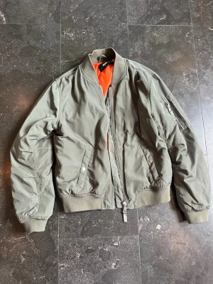 Grön bomberjacka - Ifrån bikbok, det står strl L MEN den upplevs  inte som det! Jag är 172 cm lång och brukar bära strl S på överkroppen och jag skulle säga att detta är mer jacka i strl S/M. Köpt second hand på sellpy men den ser typ helt ny ut! Jag kommer skriva strl M på jackan pga att den inte är som en L. Millitärgrön färg.