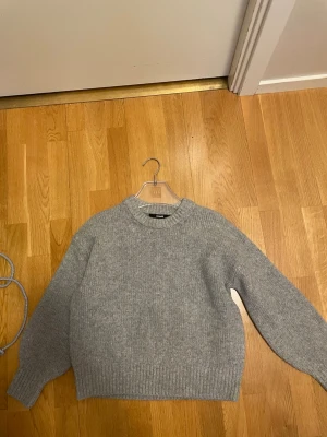 Grå stickad tröja från BikBok - Mysig grå stickad tröja från BikBok i storlek XS. Tröjan har rund halsringning, långa ärmar och ribbade muddar vid ärmslut och nederkant. Perfekt för kyliga dagar och enkel att matcha med olika outfits.har jätte små få rosa fläckar vid halsringningen. Kan kanske gå bort vid noggrann tvätt men vet ej. 
