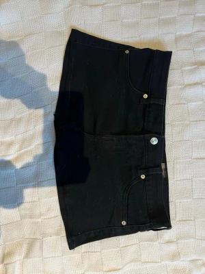 Svart mini denimkjol med fem fickor - Säljer en svart minikjol med klassisk femficksdesign, knapp och dragkedja framtill samt bakfickor. Shortsen har en enkel och stilren look som funkar till det mesta och är perfekta för sommaren.