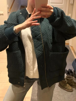 Mörkgrön quiltad bomberjacka - Mörkgrön quiltad bomberjacka med stora fickor framtill och ribbade muddar vid ärmar och nederkant. Jackan har dragkedja och en oversized passform 💚