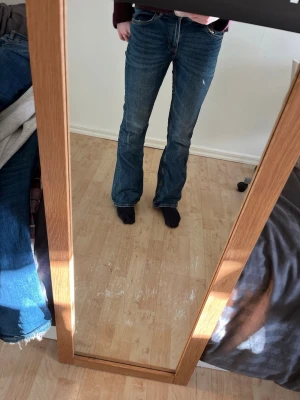 Blå bootcut jeans med låg midja - Säljer ett par klassiska blå bootcut jeans med låg midja och femficksmodell. Jeansen har en lätt tvättad look och är tillverkade i denim med lite stretch för skön passform. Perfekta för en avslappnad och trendig stil.