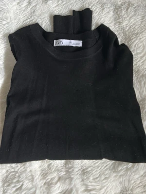 Svart stickad tröja från Zara - Snygg svart stickad tröja från Zara med rund halsringning och långa ärmar. Ärmsluten har fyra guldfärgade knappar som ger en extra detalj. Tröjan är i mjukt material och har ribbade muddar vid ärmslut och nederkant.