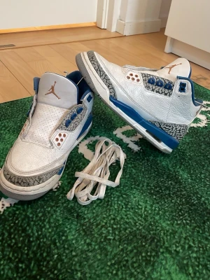Air Jordan 3 Retro Wizard - Säljer ett par Air Jordan 3 Wizard sneakers i vitt läder med blå detaljer och klassiskt elephant print runt tå och häl. Skorna har blå innersula, vita skosnören och Jumpman-logga på plösen och hälen. Perfekta för dig som gillar ikoniska och sportiga sneakers. Storlek 36,5. Växte ur dem ett tag sedan men de är i utmärkt skick! Köptes från Nike (finns många replikor som säljs här på plick). Pris kan möjligen diskuteras! - Noah😁