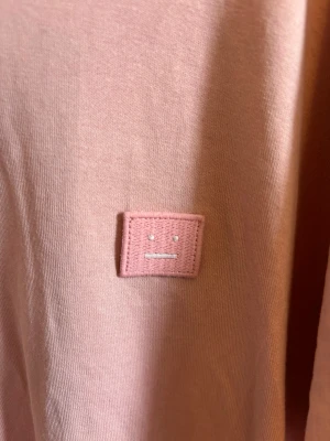 Rosa t-shirt från Acne Studios - Säljer en rosa t-shirt från Acne Studios med det ikoniska ansiktslogotypen på bröstet. Orginalpris: 2700kr